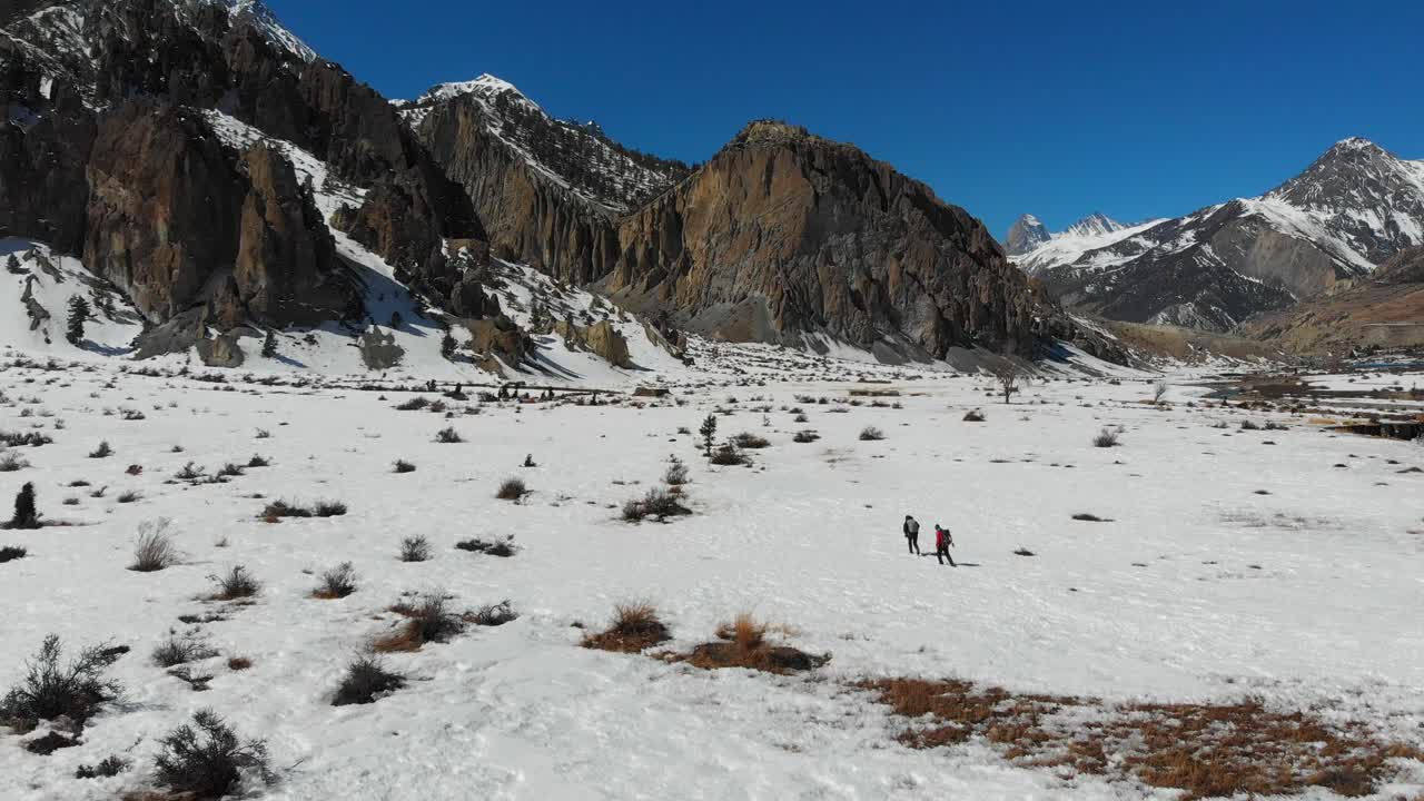 Aerial slider shot of two people walking on a snow-covered field in Manang, Nepal