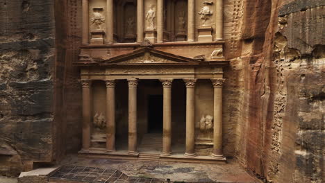 Ascending-aerial-view-of-a-person-in-front-of-the-Treasury,-Al-Khazneh-in-Petra,-Jordan