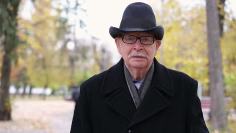 the senior walks in the autumn park he is dressed in a black coat and a hat autumn fashion clothes the senior walks in the autumn park he is dressed in a black coat and a hat autumn fashion clothes for the elderly
