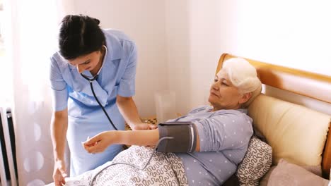 nurse checking blood pressure of senior woman in bedroom