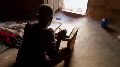vista trasera de un joven africano escribiendo en un cuaderno durante el día en el pueblo de wulugu, ghana