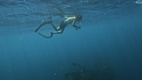 Male-free-diver-in-the-blue-ocean,-looking-for-the-liberty-shipwreck-and-exploring-under-water-world,-copy-space-and-slow-motion