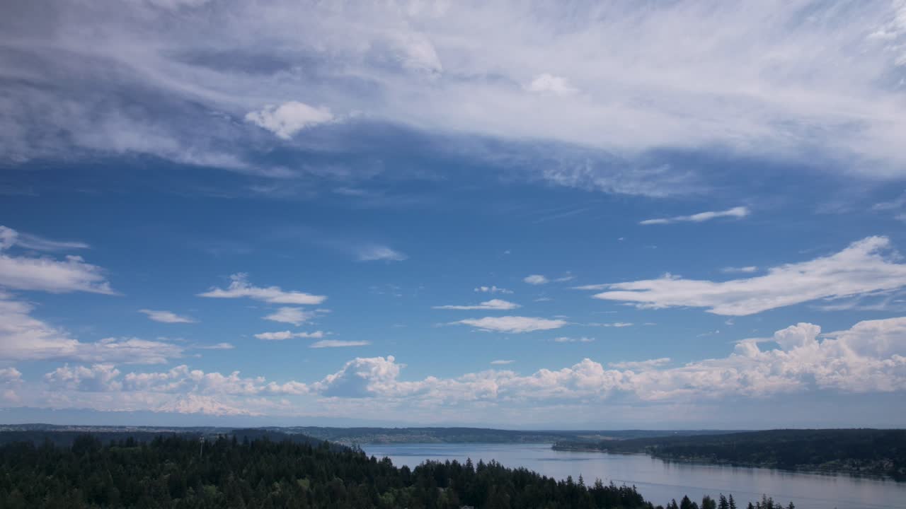 High cirrus clouds slowly move across a brilliant blue sky, reflecting off calm waters, aerial hyper-lapse