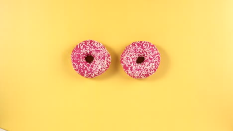 female hand remove two pink frosted donuts with sprinkles on a bright yellow background. ideal for dessert-themed content, food photography, or vibrant lifestyle visuals with a fun, colorful setup.