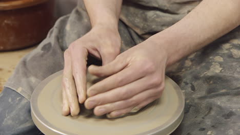 las manos de un alfarero hacen una jarra en un torno de alfarero