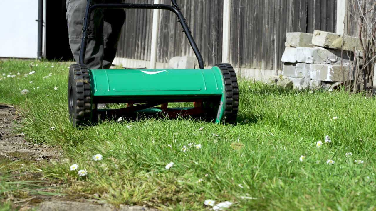 vista de bajo ángulo del jardinero usando cortadora manual en un día soleado