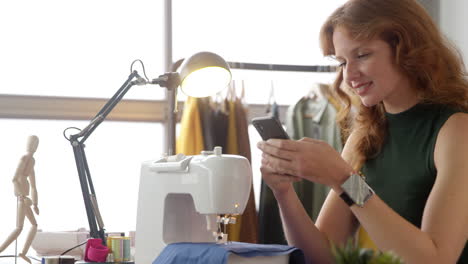 propietaria de un negocio de moda usando el teléfono móvil en la máquina de coser en el estudio