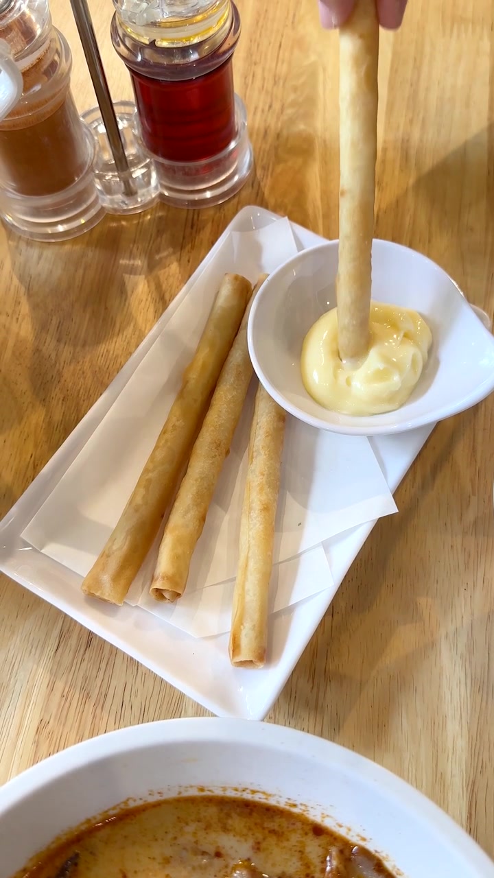 Tangan mengambil lumpia, mencelupkannya ke dalam saus, dalam pencahayaan restoran yang terang, tampilan kamera dari atas.