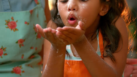 girl blowing flour with her mother in kitchen