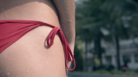 slim girl ties up red swimsuit stripes against resort hotel