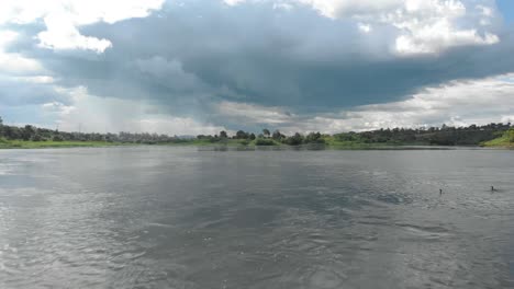 Ein-Niedriger-Fliegender-Schuss-über-Dem-Wasser-Des-Nils-Mit-Kleinen-Wellen-Im-Wasser-Und-Großen-Sturmwolken-Am-Himmel