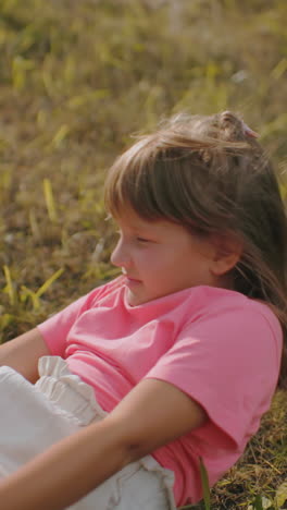 joven con camisa rosa yace en la hierba con los brazos extendidos, mirando hacia el cielo en un campo pacífico, la suave luz dorada del sol destaca su postura relajada, con el primo parcialmente visible en primer plano