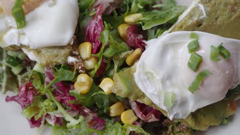 close up of avocado toast with poached eggs, corn, and greens