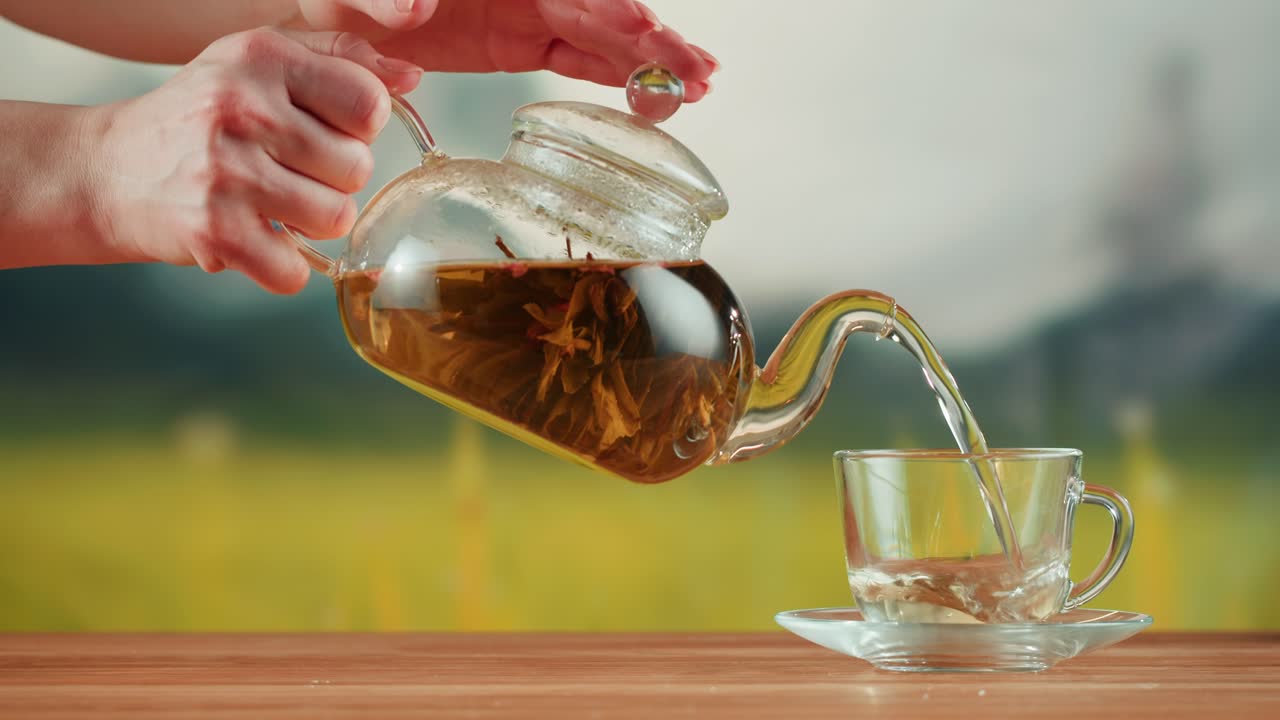 Hands Pouring Blooming Tea from a Glass Teapot into a Transparent Cup