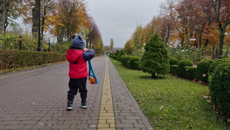 pretty kid wearing warm clothes plays with a toy outdoors. walk in the beautiful park in autumn. low angle view.