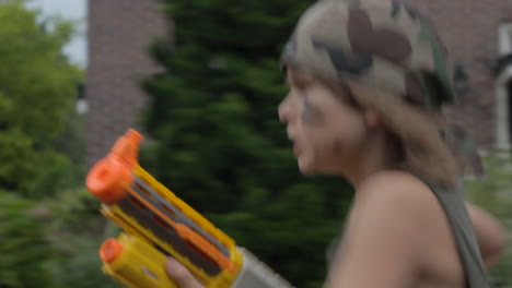 young boy playing soldier with toy gun running through beautiful suburban neighborhood