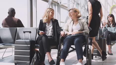 businesswoman in airport departure lounge travelling with disabled colleague in wheel chair - shot in slow motion