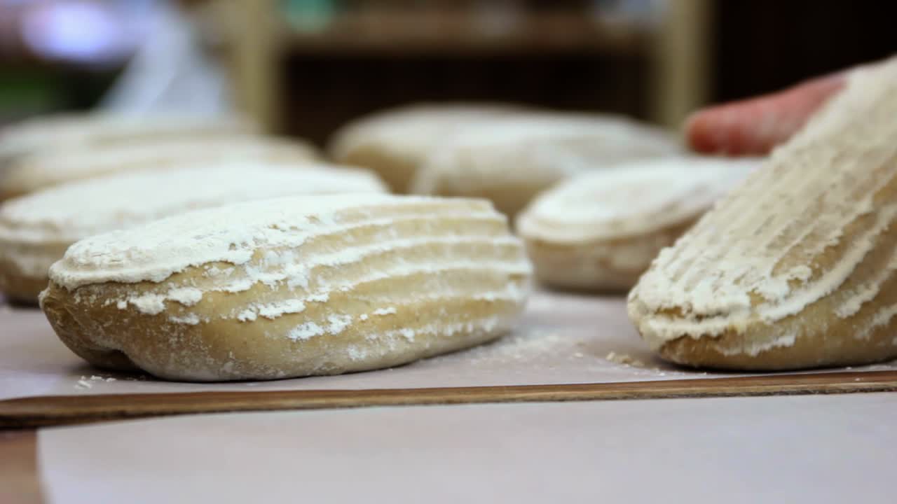 Baker lining up proofed bread dough for the oven, close