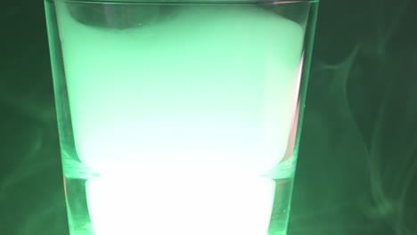 Macro-of-a-white-smoke-flying-inside-a-glass-or-glass-container-with-green-light