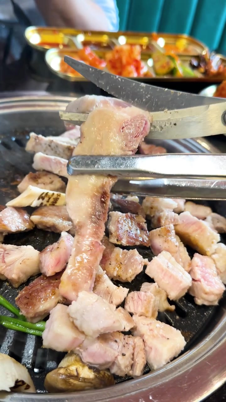 Main coupant de la poitrine de porc avec des ciseaux sur un grill de table, sous un éclairage vif, en gros plan.