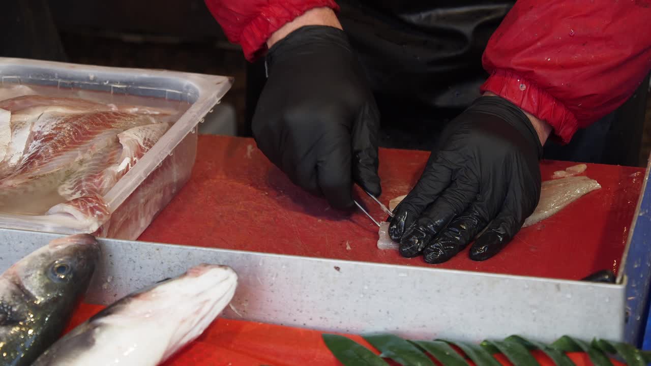 un hombre con guantes negros preparando pescado fresco para la venta en un mercado de mariscos