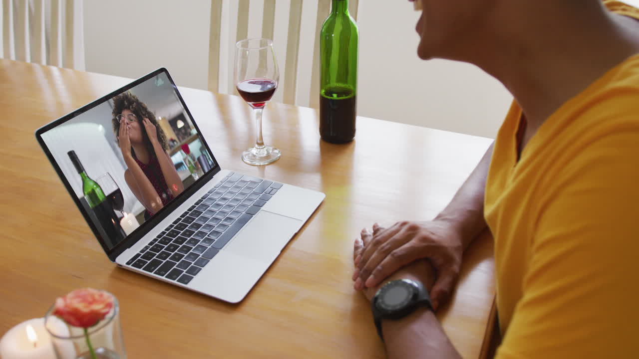 Biracial man sitting at table using laptop making video call with female friend