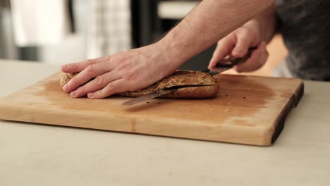 white man slicing through brown baguette with serrated knife on kitchen countertop