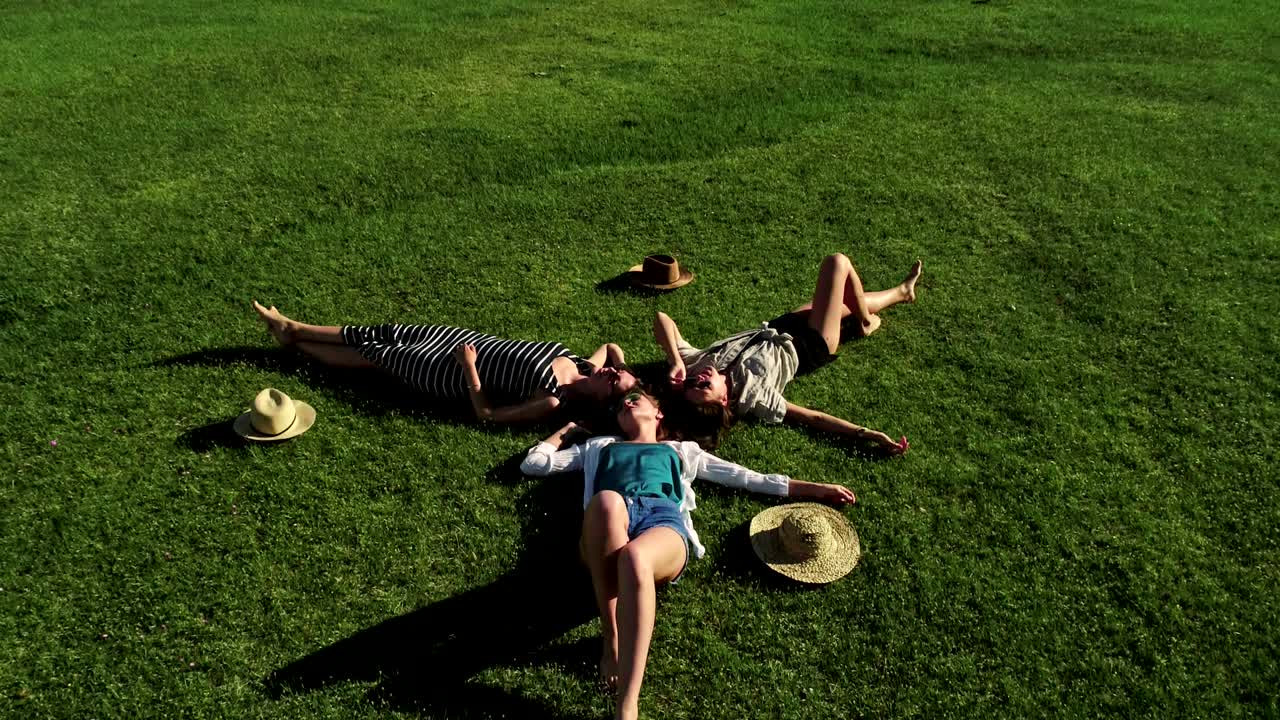 초록 잔디 위에 누워있는 세 명의 매력적인 소녀들이 잔디에서 즐거움을 즐기고 있습니다.