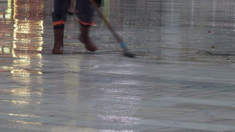 two workers sweeping a wet street