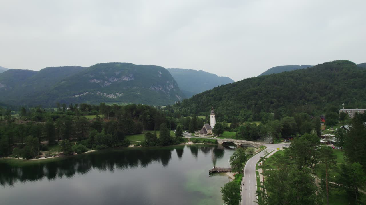 Ripresa con drone sul lago di Bohinj in Slovenia con una chiesa e montagne sullo sfondo al tramonto
