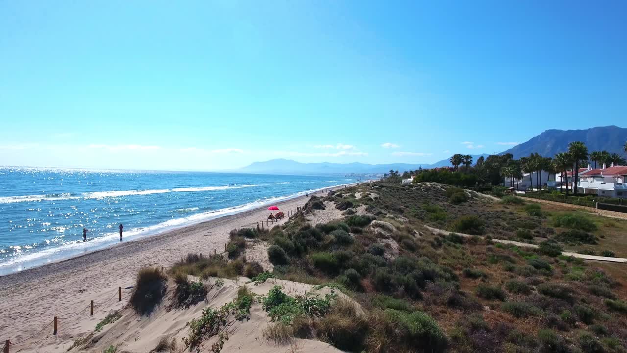 drone volando sobre dunas de arena junto a una playa soleada