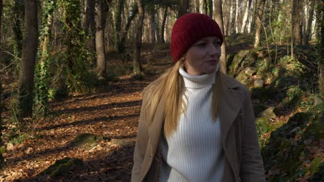 woman in red hat and white turtleneck sweater walks in autumn forest, dolly out