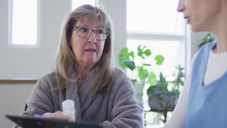 mujer mayor sosteniendo un contenedor de medicamentos hablando con una trabajadora de salud