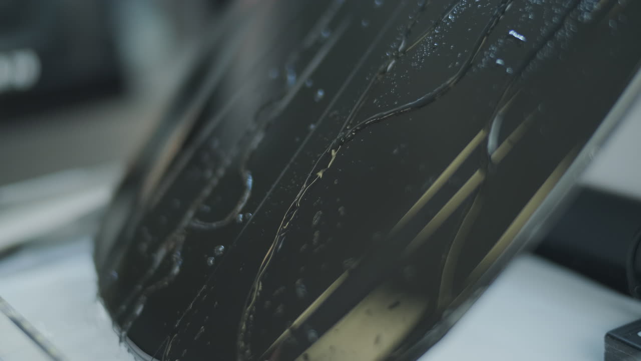 Detailní záběr vodních kapek tekoucích po tmavém povrchu