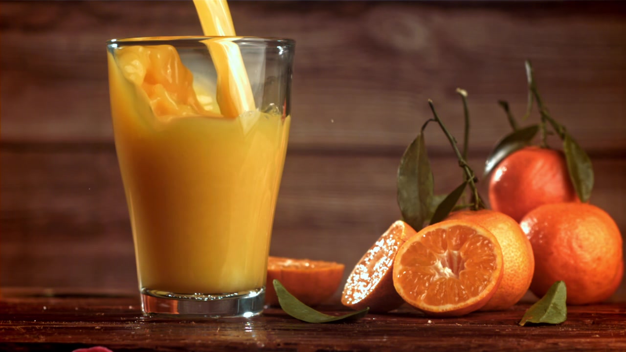 Succo d'arancia fresco versato in un bicchiere con arance intere e a fette