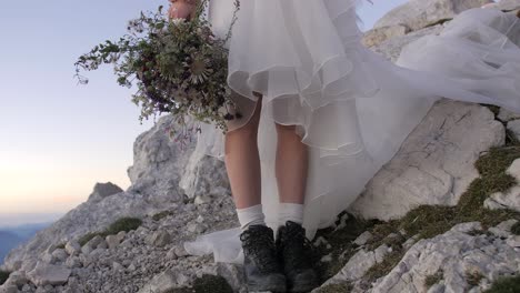 novia en las montañas con vestido de novia y botas negras con ramo de flores silvestres