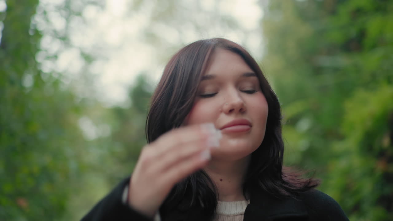 숲 속에서 책 페이지를 넘기며 천천히 거닐고, 부드러운 미소로 주변을 둘러보는 여성 탐험가의 미디엄 샷, 가을의 녹음과 보케, 평화로운 야외 산책, 신중한 호기심