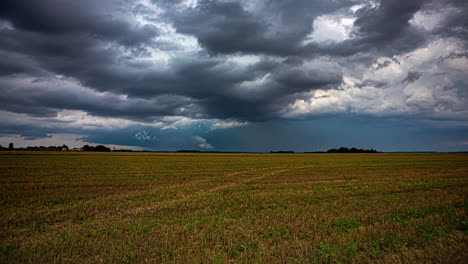 Dark-extreme-rain-clouds-flowing-above-rural-landscape-with-farmers-working,-time-lapse