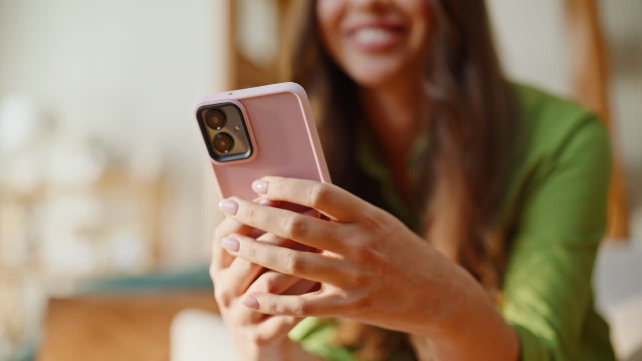 Donna a casa che invia messaggi con lo smartphone seduta comodamente su un divano morbido. Ragazza sorridente