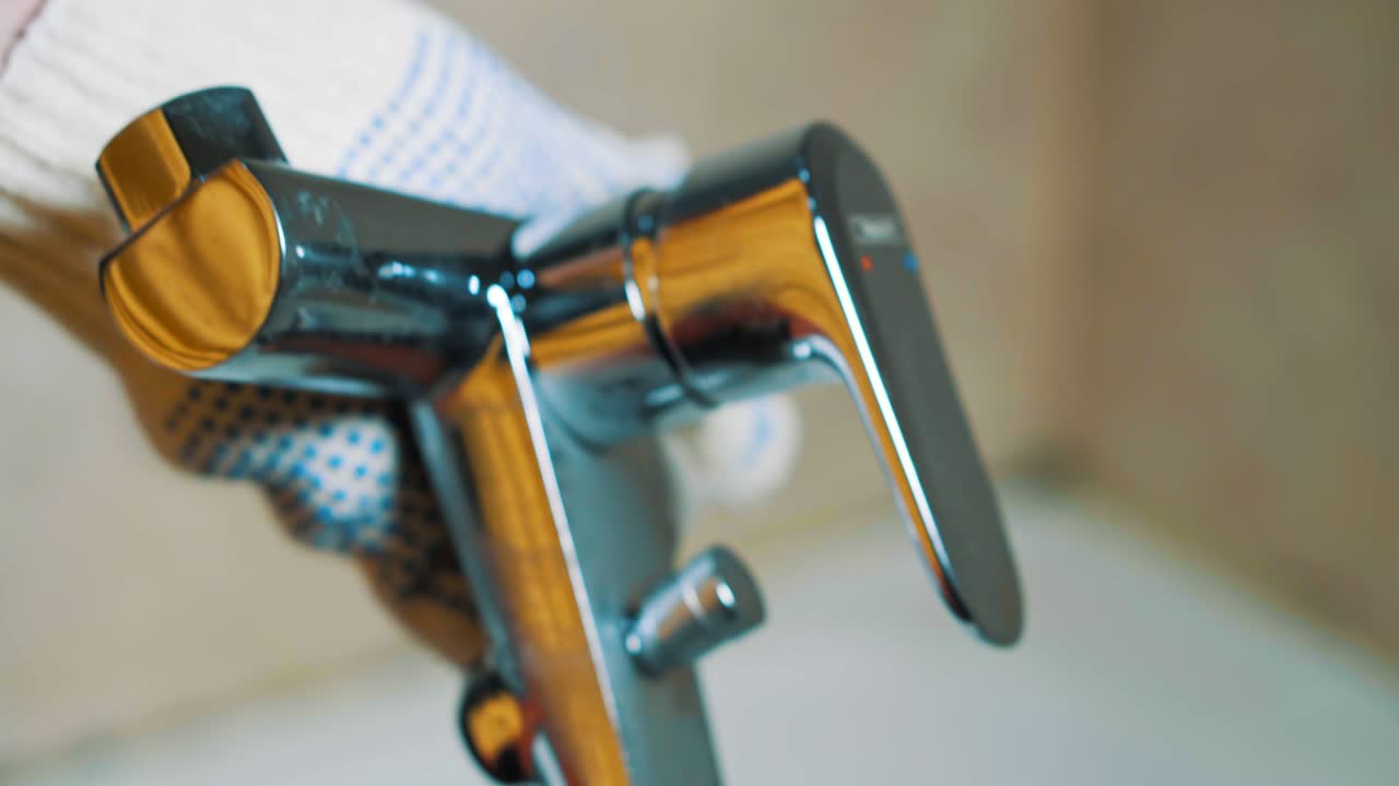 primer plano de las manos con guantes del fontanero sosteniendo un grifo de agua.