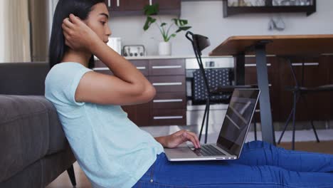 Mixed-race-gender-fluid-person-sitting-on-floor-and-using-laptop-at-home