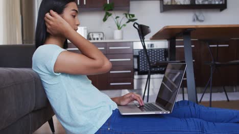 Mixed race gender fluid person sitting on floor and using laptop at home