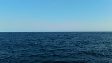 aerial pullback above calm ocean with small white caps on top and soft blue gradient sky horizon