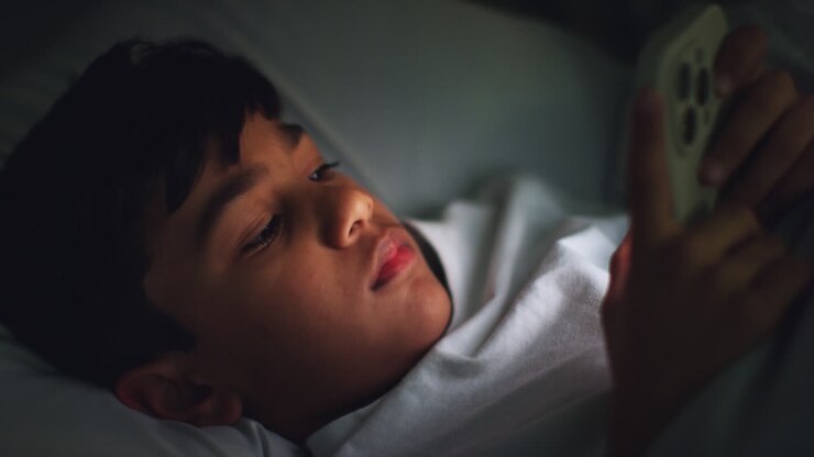 Ragazzo stanco nella sua camera da letto a casa sdraiato a letto che usa il cellulare per mandare messaggi di notte 2