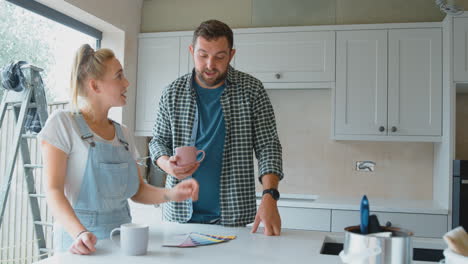 Pareja-Renovando-La-Cocina-En-Casa-Mirando-Muestras-De-Pintura-En-Una-Pausa-Para-El-Café