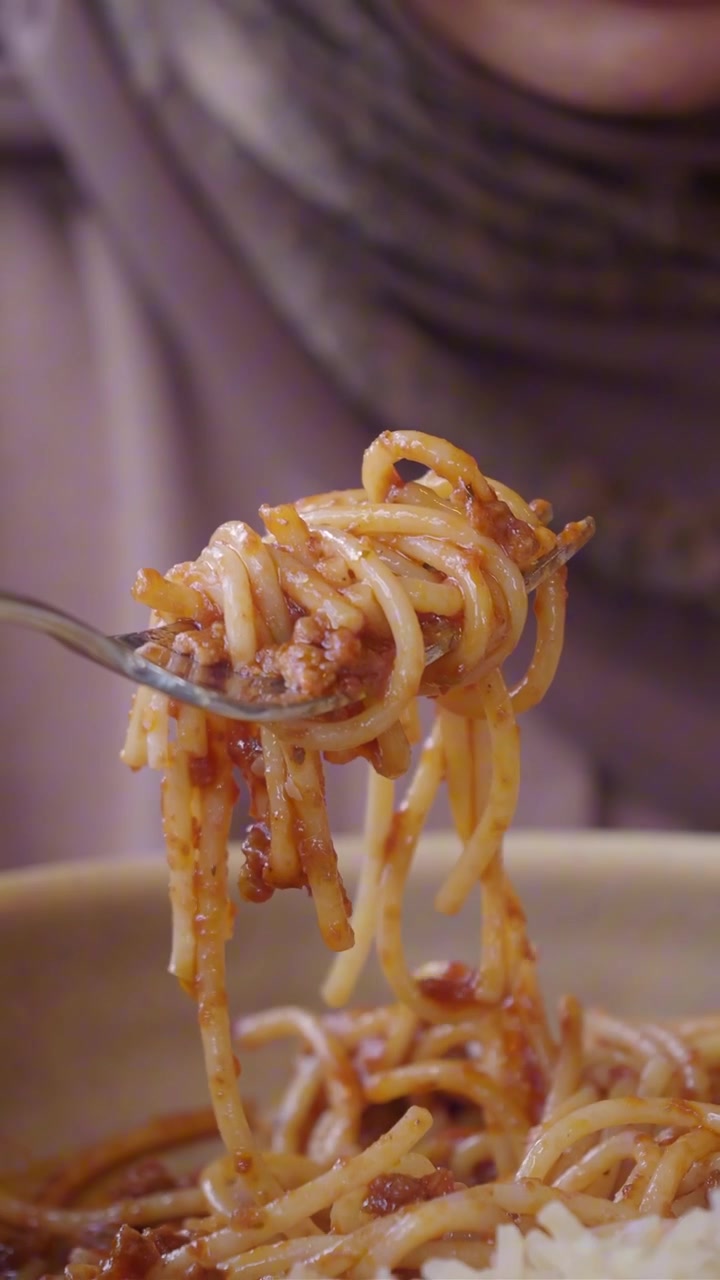 Persona che avvolge gli spaghetti al ragù con una forchetta.