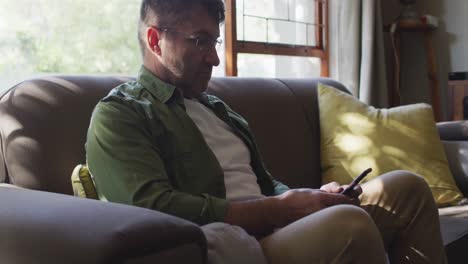 Caucasian-man-sitting-on-sofa,-using-smartphone-at-home