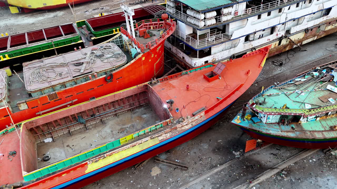 Cinematic aerial drone shot flying toward a welder working on a docked cargo ship in Dhaka, Bangladesh.
