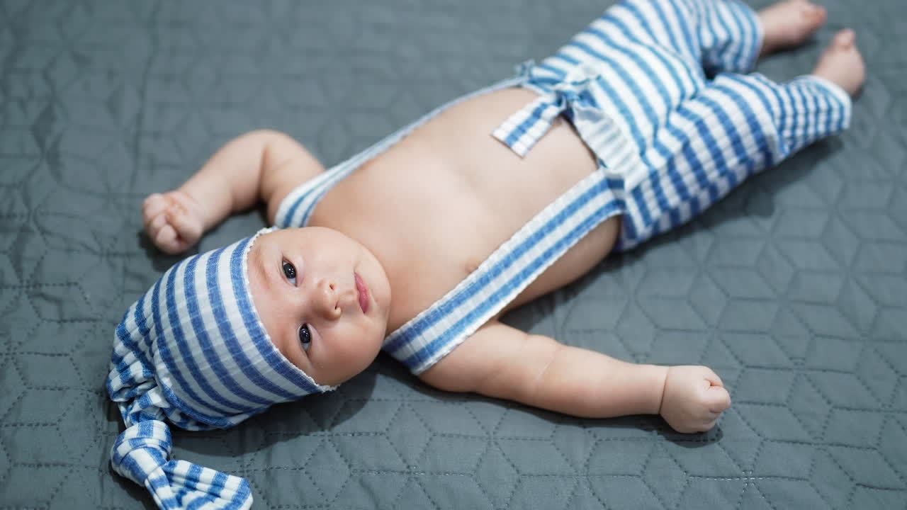 Little boy in a funny striped costume lying calmly on the bed. Baby with naked belly resting on grey background. Close up.