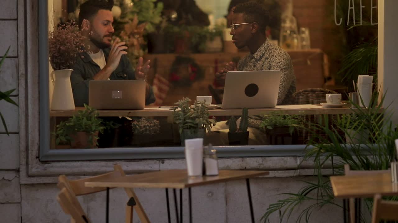 Men talking and working with laptops in coffee shop